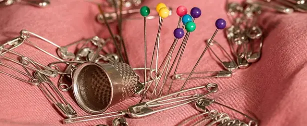 Dé à coudre, épingles et épingles à nourrice sur un tissu rose